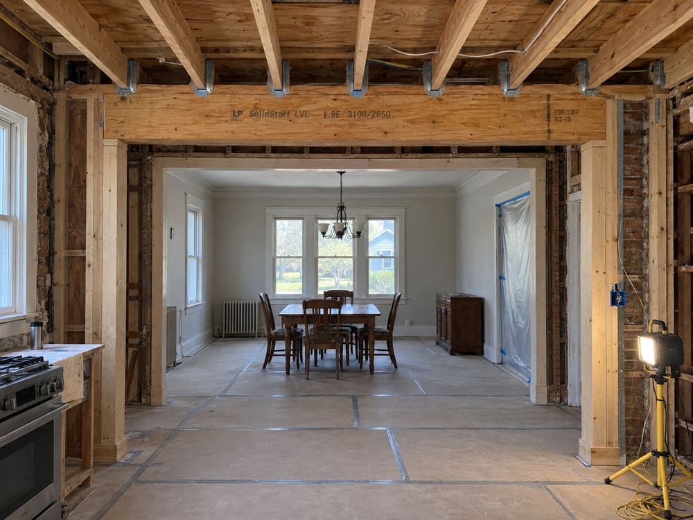 Engineered lumber beam installed over a new opening between a kitchen and dining room, with joists hung from it and posts at each end
