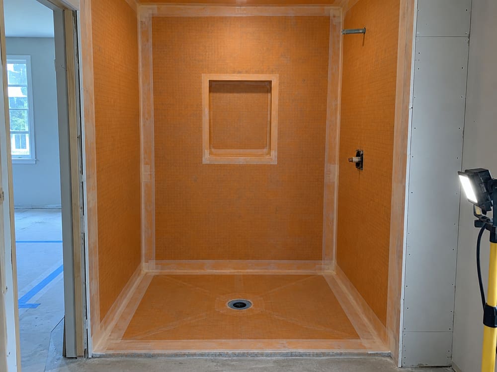 Shower under construction with a bonded waterproofing membrane over the walls and pan, seams banded at every corner and a recessed niche